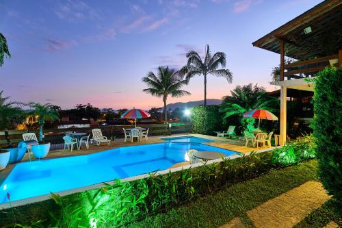 a pool with chairs and umbrellas in front of a house at Chalés Mirante da Lagoinha in Ubatuba
