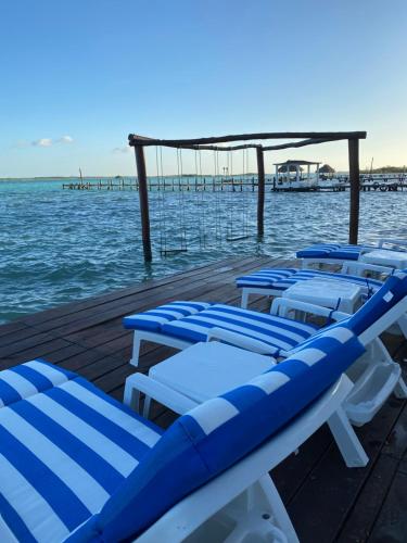 a row of blue and white chairs on a dock in the water at Hotel Aldea 19 Bacalar in Bacalar