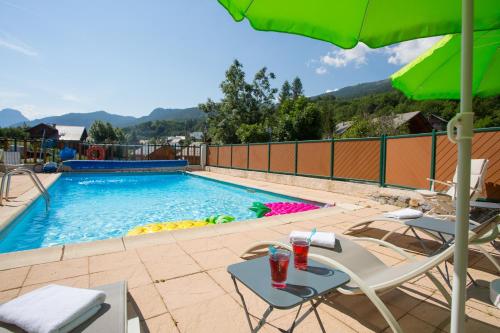 einen Pool mit einem Tisch, Stühlen und einem Sonnenschirm in der Unterkunft Hôtel Aigliere in Puy-Saint-Vincent