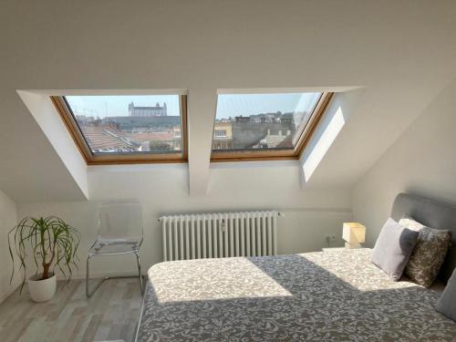 a bedroom with a bed and a chair and two windows at Queen Flat in Old Town with Castle view in Bratislava