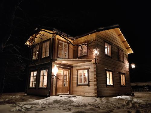una casa de madera con luces encendidas en la nieve por la noche en Aurora Nova, en Koskullskulle