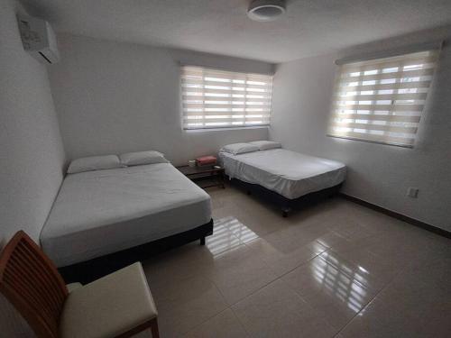 a bedroom with two beds and a chair and two windows at Un pedacito de arena en Cancún in Cancún