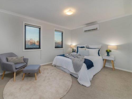 a bedroom with a bed and a chair and two windows at Merchant's Court, Quiet and Central 3 bedroom townhouse in Wangaratta