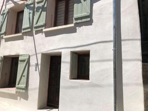 a white building with green shuttered windows and a door at Charmante maison de village avec toit terrasse in Montalba-le-Château