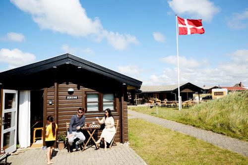 Fjand Badeby - Guesthouse, Cottages and Colony في Ulfborg: مجموعة من الناس تقف خارج كابينة مع العلم