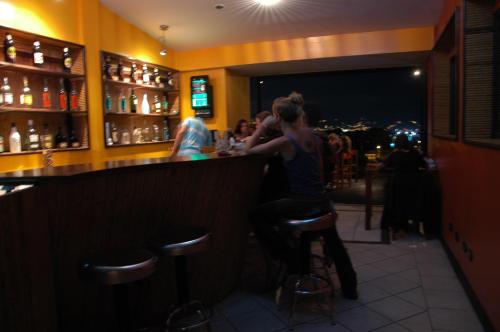 two people sitting at a bar looking at their cell phones at Alajuela Backpackers Airport Hostel in Alajuela