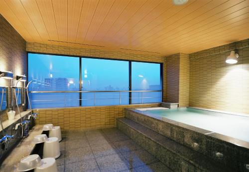La salle de bains est pourvue d'une grande baignoire et d'une grande fenêtre. dans l'établissement Toyama Manten Hotel, à Toyama