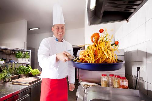 a chef in a kitchen with a pan of food at Willa Marianna in Lądek-Zdrój