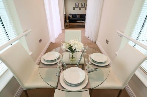 a glass table with white plates and flowers on it at Portfolio Apartments - Welwyn Business Park in Welwyn Garden City
