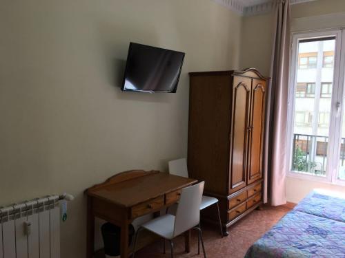 Schlafzimmer mit einem Schreibtisch und einem TV an der Wand in der Unterkunft Hostal Retiro in Madrid