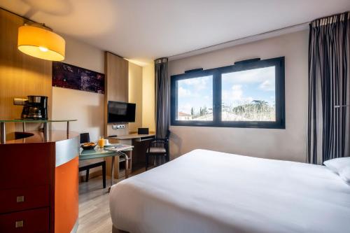 a hotel room with a bed and a desk and a window at Clarion Aparthotel Toulouse Blagnac Airport in Blagnac
