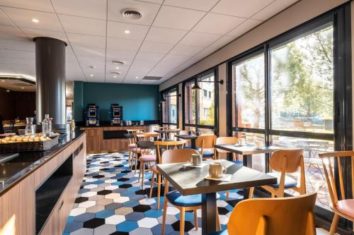 a restaurant with tables and chairs and windows at Clarion Aparthotel Toulouse Blagnac Airport in Blagnac