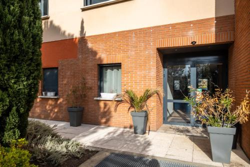 a brick building with two potted plants in front of it at Clarion Aparthotel Toulouse Blagnac Airport in Blagnac
