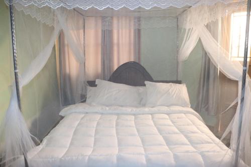a bedroom with a white canopy bed with white pillows at Jusvero Motel in Jinja