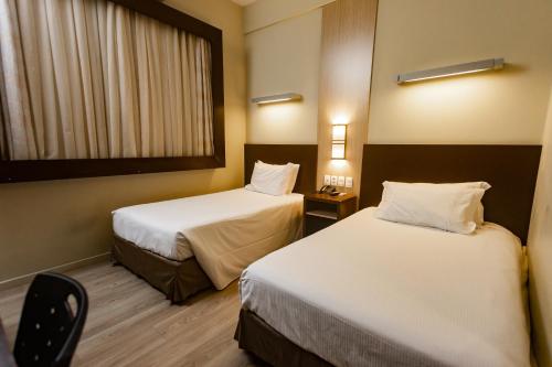 a hotel room with two beds and a chair at Master Cosmopolitan Moinhos de Vento in Porto Alegre
