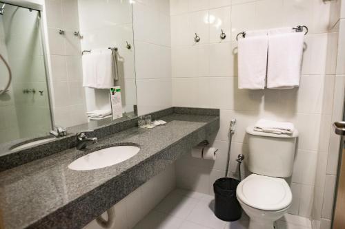 a bathroom with a toilet, sink, and mirror at Master Cosmopolitan Moinhos de Vento in Porto Alegre
