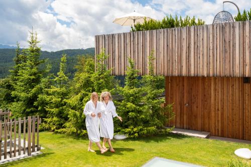 two women in white walking in a garden at Tratterhof Mountain Sky Hotel in Maranza