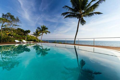 a large swimming pool next to a beach with a palm tree at Sol-lua Bungalow in Ilhabela