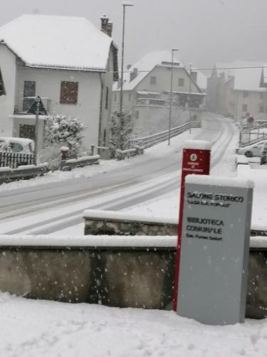 a snow covered street with a sign in the foreground at La casa del popolo in Prato Carnico
