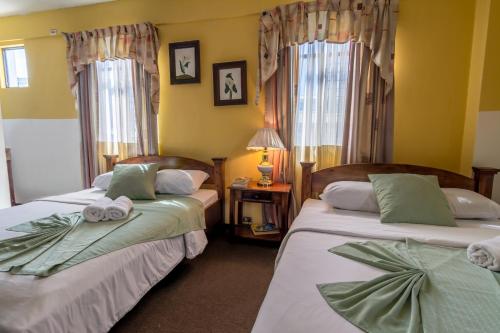 two beds in a room with yellow walls and windows at Hotel Amón Real Costa Rica in San José