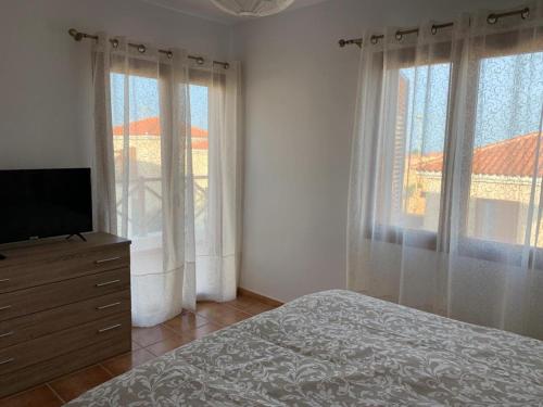 Un dormitorio con una cama y un televisor y ventanas. en Casa Los Majos, en Corralejo