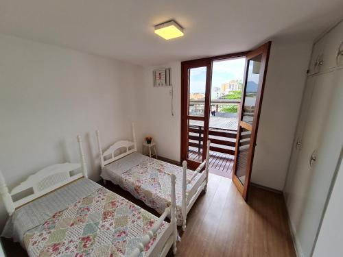 1 dormitorio con 2 camas y puerta a un balcón en Casa Super Agradável, 250 metros da praia da Areia Preta, cinco quartos com ar, wifi, garagem, completa en Guarapari