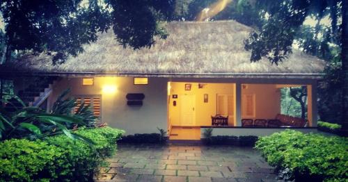 a small white house with a thatched roof at Davis Farm House in Marayoor