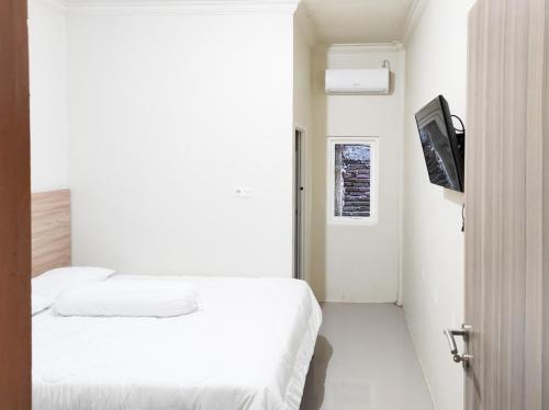 um quarto branco com uma cama e uma televisão em RedDoorz Syariah at Karema Area Mamuju em Karema