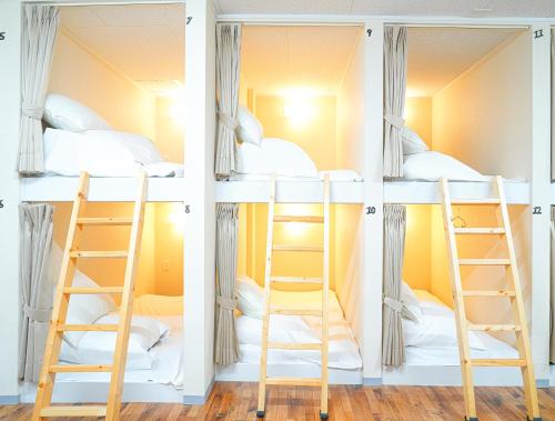 three bunk beds in a room with a ladder at ONE HOSTEL Himeji ワンホステル姫路 in Himeji