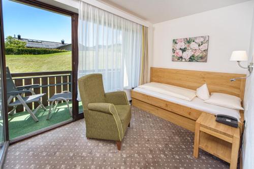 a hotel room with a bed and a chair and a balcony at Interest Vitalhotel - Partnerbetrieb von Oberstaufen PLUS in Oberstaufen