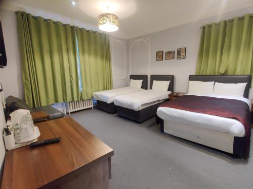 a room with two beds with green curtains and a desk at Chelsea House Hotel - B&B in London