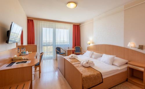 ハイドゥソボスローにあるHotel Barátságの大きなベッドとデスクが備わるホテルルームです。