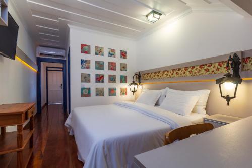 a hotel room with a bed, desk, and a painting on the wall at Pousada Aconchego in Paraty