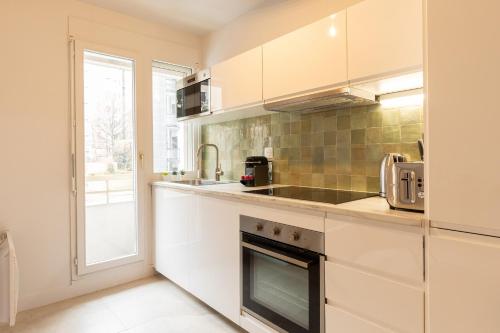 une cuisine avec des armoires blanches, un évier et une fenêtre dans l'établissement DIFY Louis Blanc - Brotteaux, à Lyon