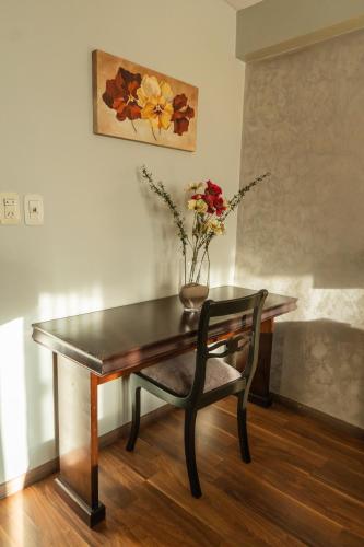 a table and a chair with a vase of flowers at Hotel Embajador in San Miguel de Tucumán