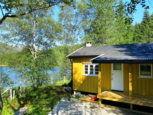 uma pequena casa amarela com um alpendre ao lado de um lago em Holiday Home Oddbu - SOW103 by Interhome em Åseral