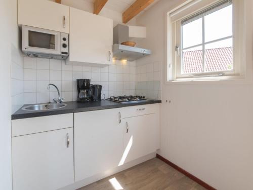een keuken met witte kasten, een wastafel en een raam bij Holiday Home Zeeuwse Cottage Wemeldinge-3 by Interhome in Wemeldinge
