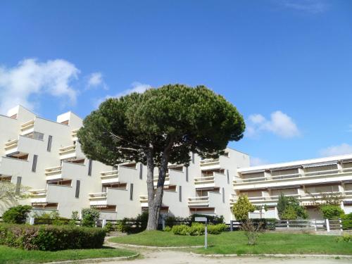 un bâtiment blanc avec un arbre devant lui dans l'établissement Apartment Le Serpent de Mer-7 by Interhome, au Grau-du-Roi