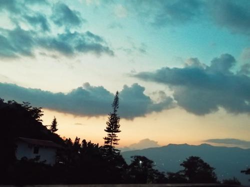 a sunset with a tree in front of a building at Glamping Montaña Escondida in Fusagasuga