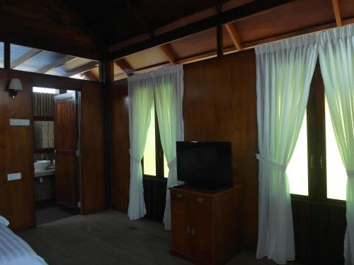 a bedroom with a bed and a tv and curtains at The Gemalai Village in Pantai Cenang