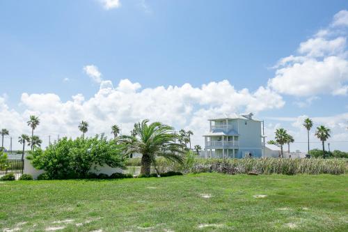 a large white house with palm trees and a field at Bella Vista & Four Winds House in Padre Island