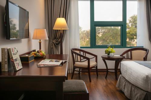 a hotel room with a desk and a bed and a table and chairs at The Tray Hotel Hai Phong in Hai Phong