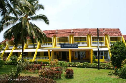 a yellow building with a palm tree in front of it at Colva Residency in Colva