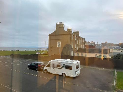 une camionnette blanche garée sur un parking avec une voiture dans l'établissement holiday apartment, à Ardrossan