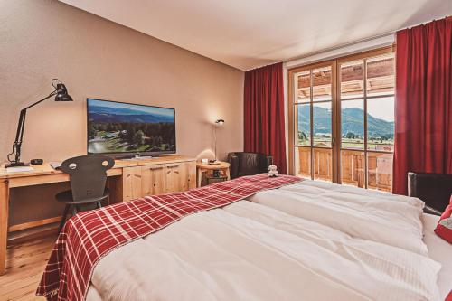 Schlafzimmer mit einem Bett, einem Schreibtisch und einem TV in der Unterkunft Das Achental Resort in Grassau