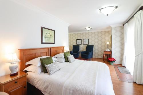 a bedroom with a large white bed and chairs at A Tuscan Villa Guest House in Fish hoek