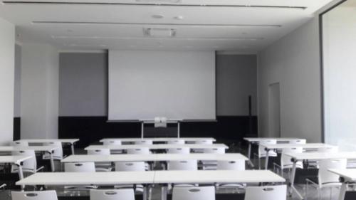 un aula vacía con mesas blancas y una pantalla de proyección en M2 Hotel Waterside, en Phayao