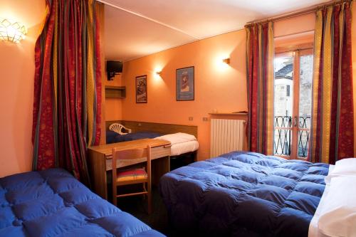 Schlafzimmer mit blauen Betten, einem Schreibtisch und einem Fenster in der Unterkunft Hotel La Piazzetta in Limone Piemonte