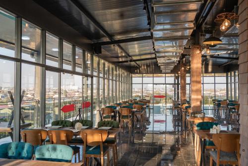 un ristorante con tavoli, sedie e finestre di Rayyan Hotel & SPA Tashkent a Tashkent