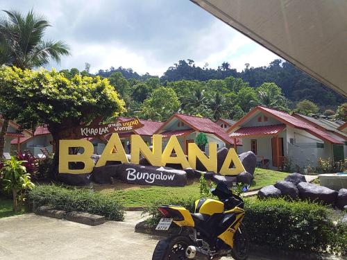 une moto garée devant un panneau bannana dans l'établissement Khaolak Banana Bungalow, à Khao Lak